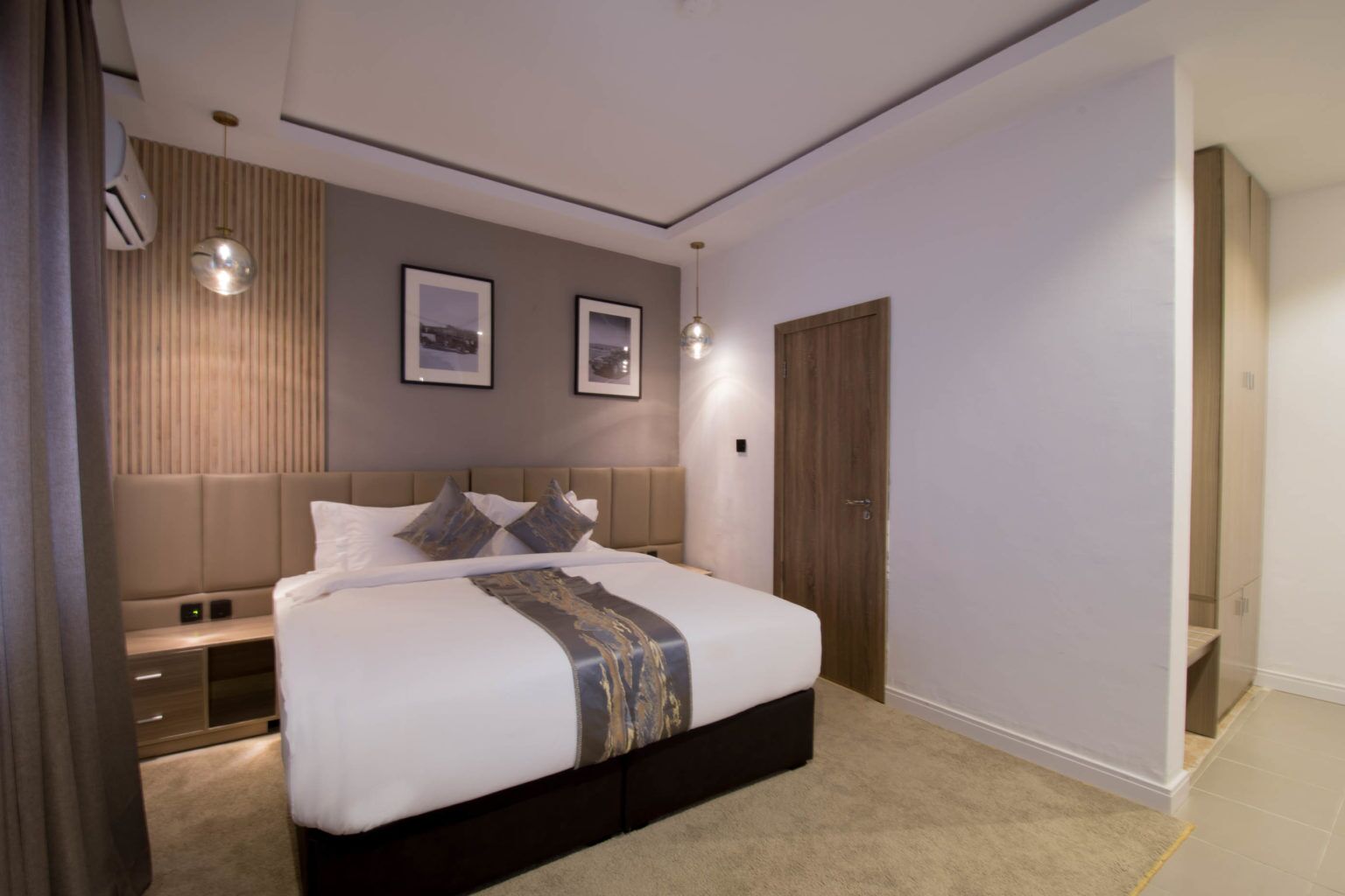 A modern bedroom with a large bed, bedside tables, a wardrobe, and a door.