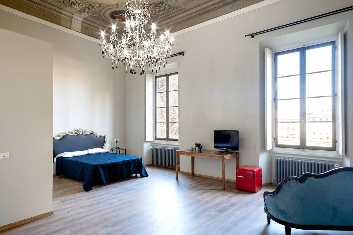 A bedroom with a bed, a television, a red suitcase, and a chair.