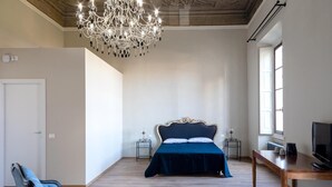 A bedroom with a large bed, a chandelier, a desk, and a chair. - B&B Stupido Hotel (Florence)