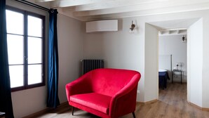 A room with a red armchair, a radiator, a window with curtains, and a hallway leading to another room. - B&B Stupido Hotel (Florence)