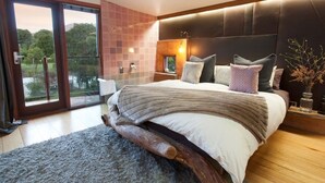A modern bedroom with a large bed, a wooden headboard, and a view of a garden through a sliding glass door. - Eco Villa Mt Beauty Near Falls Creek & Bright (Tawonga South)