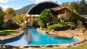 A swimming pool with a wooden deck, surrounded by rocks and plants, and a covered area with a curved roof. - Eco Villa Mt Beauty Near Falls Creek & Bright (Tawonga South)