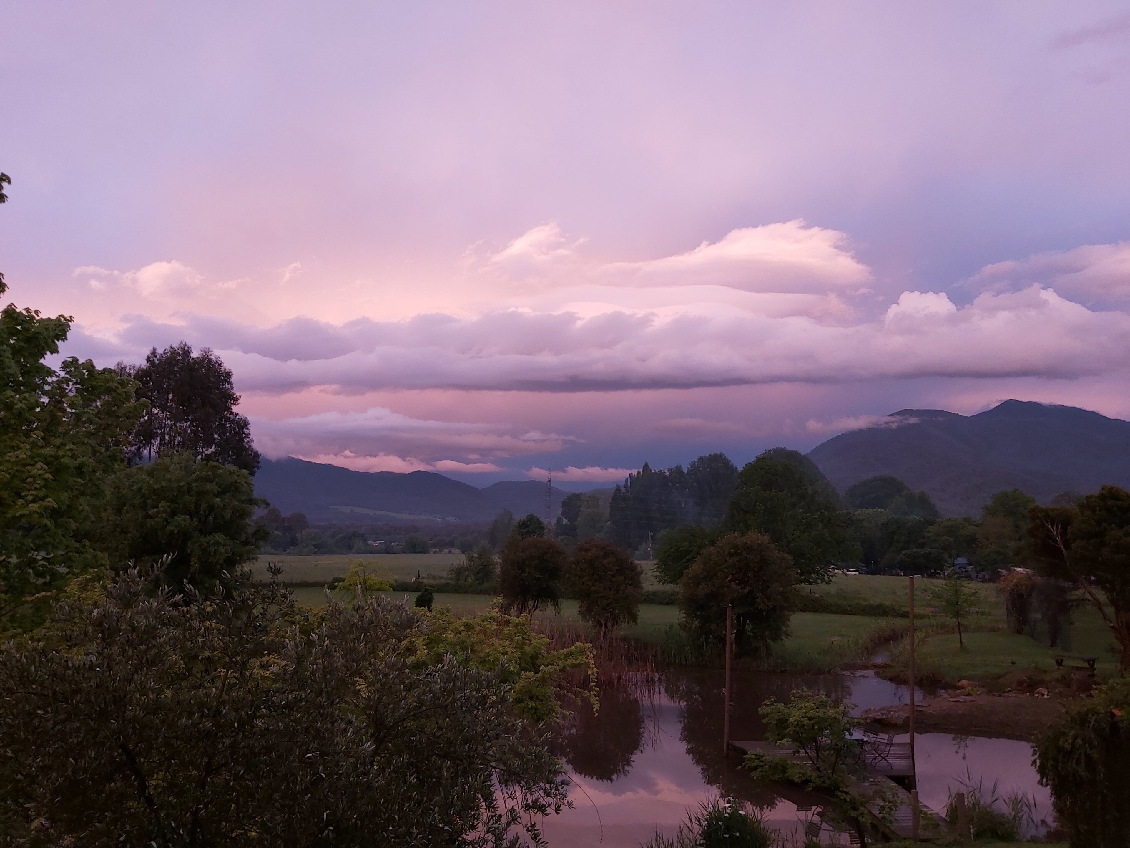 Paisagem tranquila com um lago, árvores e montanhas sob um céu rosado.