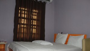 A bedroom with a bed, a nightstand, and a window with curtains. - Ayoluyem Hotel (Port Harcourt)