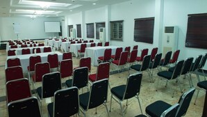 A conference room with rows of tables and chairs, white walls, and ceiling lights. - Ayoluyem Hotel (Port Harcourt)