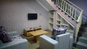 A living room with a sofa, a coffee table, a TV mounted on the wall, and a staircase with a railing. - Ayoluyem Hotel (Port Harcourt)
