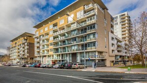 A multi-story residential building with balconies, a parking lot, and a clear sky. - Spacious 1-Bedroom Apartment With Parking (Canberra)