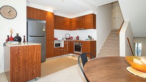 A modern kitchen with wooden cabinets, a stainless steel refrigerator, and a dining area with a wooden table and chairs. - Spacious 1-Bedroom Apartment With Parking (Canberra)