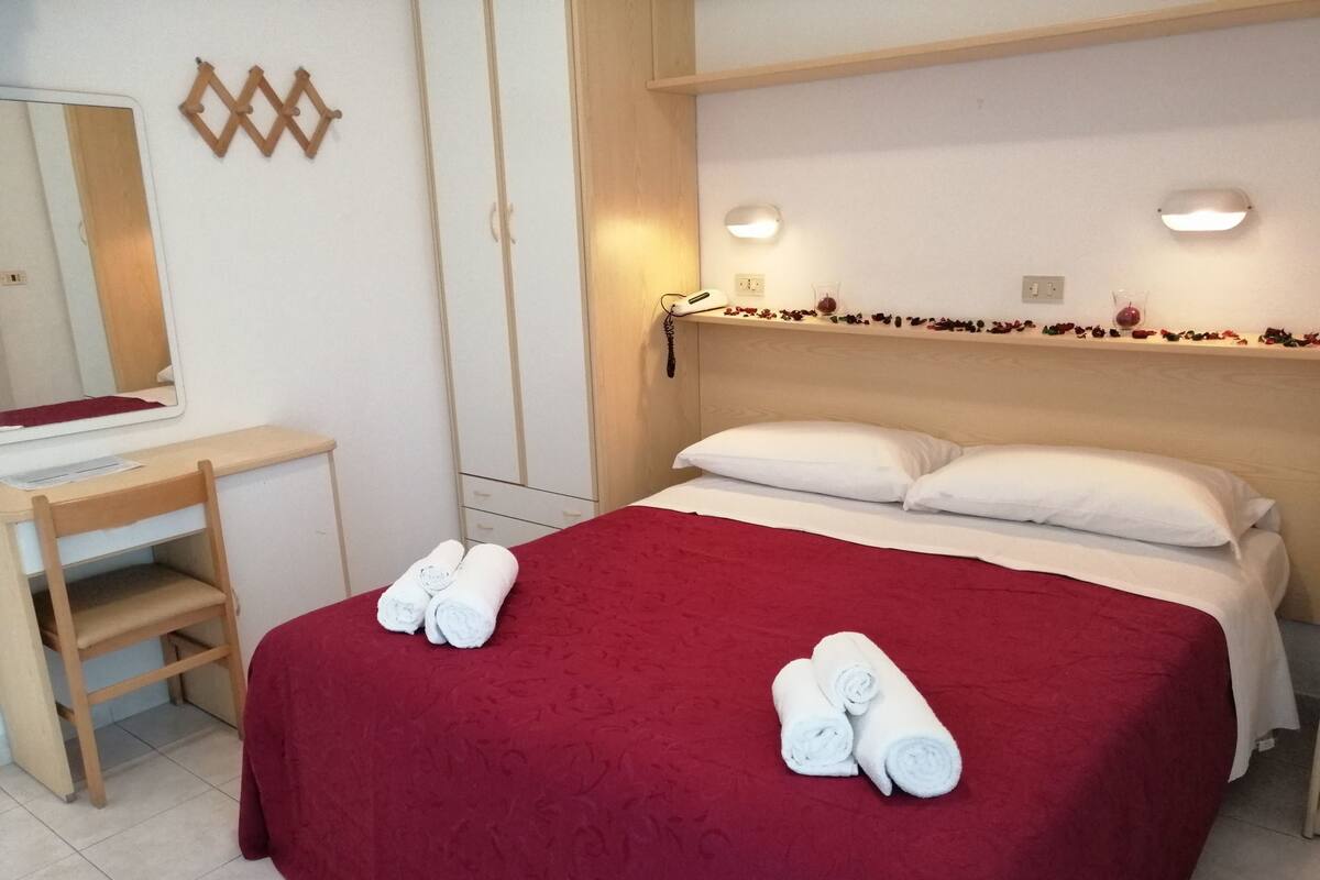 Une chambre d’hôtel avec un lit, un bureau et un miroir. Il y a des serviettes sur le lit.