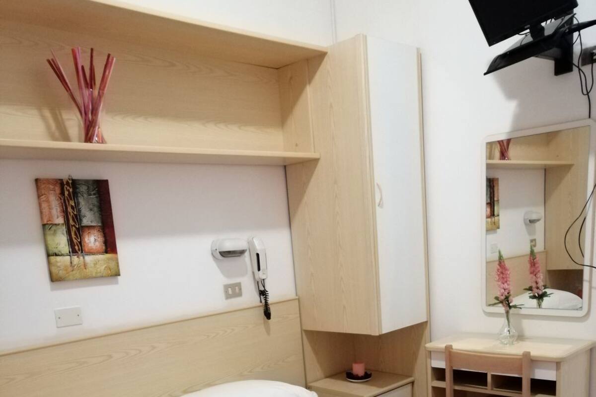 Une chambre d’hôtel comprenant un lit, une table de chevet, un miroir, un téléphone et une étagère avec des objets décoratifs.