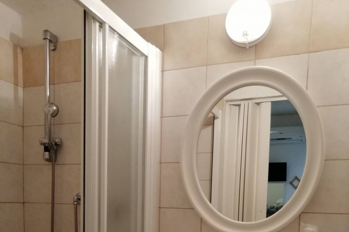 Une salle de bain avec une douche à parois de verre, un lavabo sur colonne et un miroir avec une étagère au-dessus.