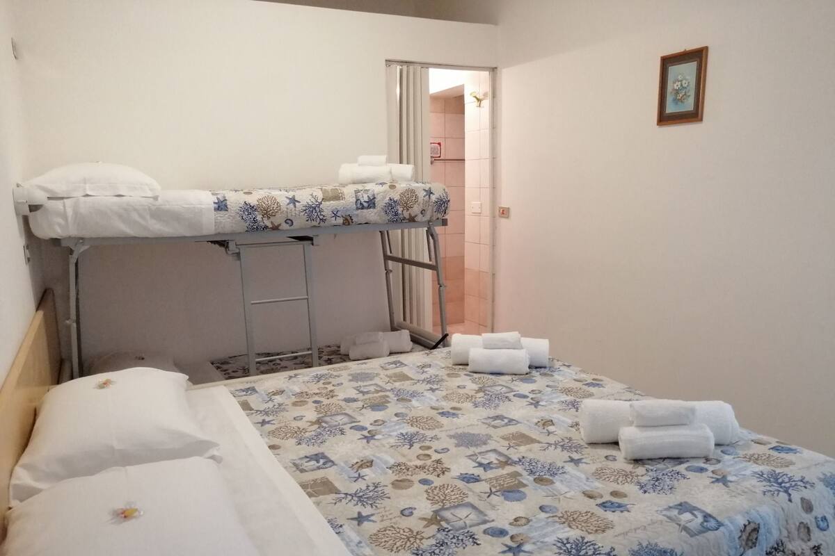 Un lit superposé avec une couvre-lit et des oreillers à motifs, une petite armoire et une porte donnant sur une salle de bain.