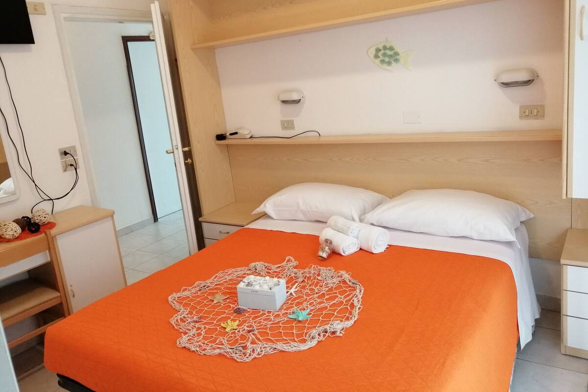 Une chambre d’hôtel avec un lit, une table de chevet, un petit bureau et une étagère.