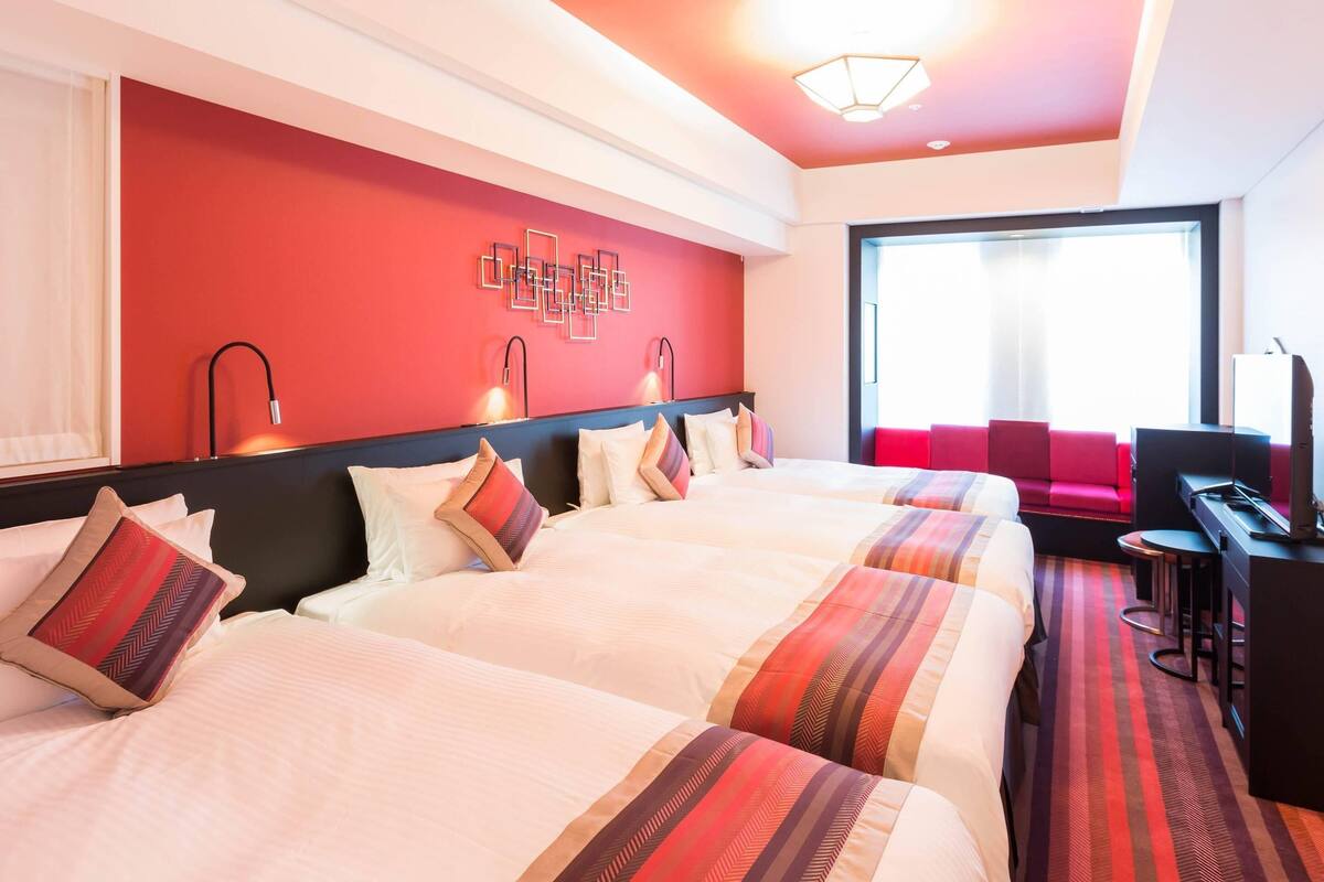 Une chambre d’hôtel avec deux lits, un bureau, une chaise et une grande fenêtre.