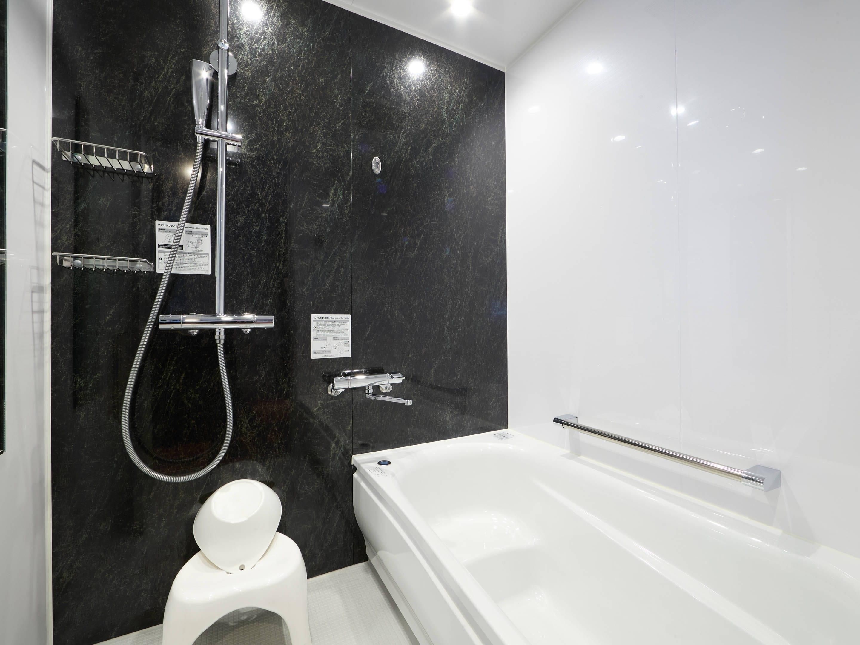 Un baño moderno con pared de mármol negro, una bañera blanca y ducha con cabezal de ducha manual.