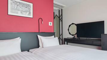 A hotel room with a bed, a flat-screen TV, a bedside table, a mirror, and a red accent wall.