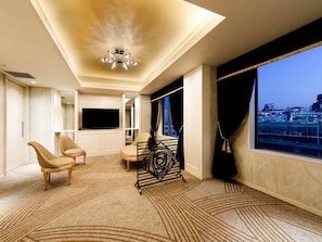 Habitación de hotel con un ventanal grande, ventilador de techo, televisor de pantalla plana y zona de estar con sillas y una mesa pequeña.