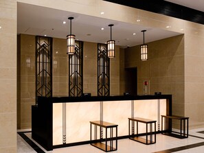 Un comptoir d’accueil avec trois suspensions lumineuses, un espace d’attente et un mur en marbre.