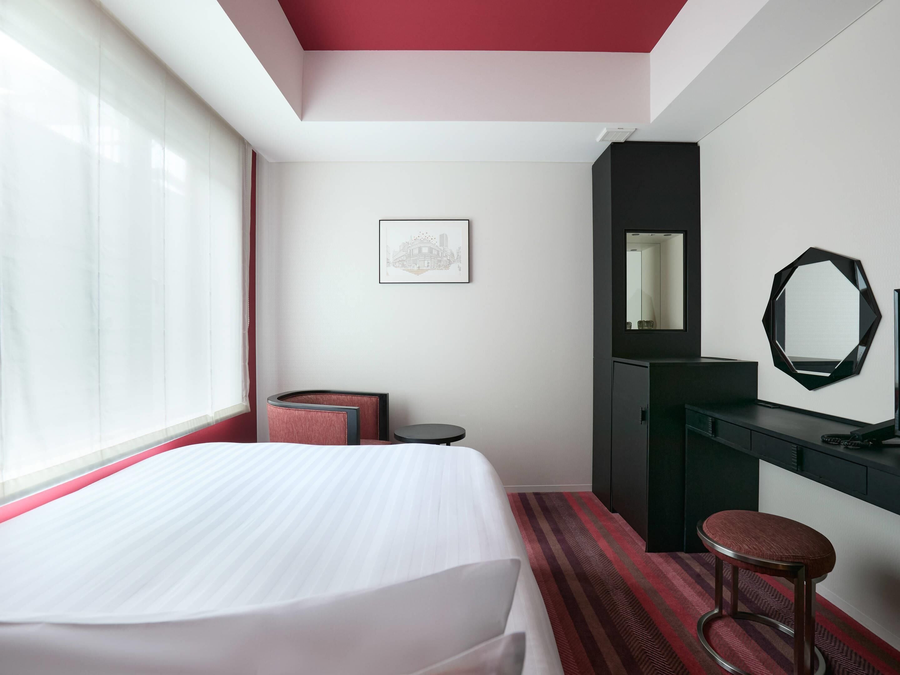 A hotel room with a bed, a desk, a chair, a mirror, and a window.