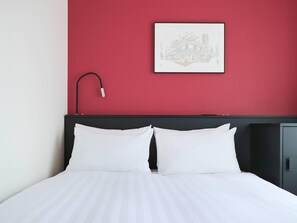 Una cama bien hecha con sábanas blancas, cabecera negra y una lámpara de noche.