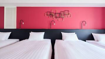 Habitación de hotel con dos camas, una pared de acento roja y una lámpara con diseño geométrico.