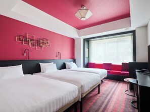 Ein Hotelzimmer mit zwei Betten, einem Schreibtisch, einem Stuhl, einem großen Fenster mit Vorhängen und einer Wanddekoration.