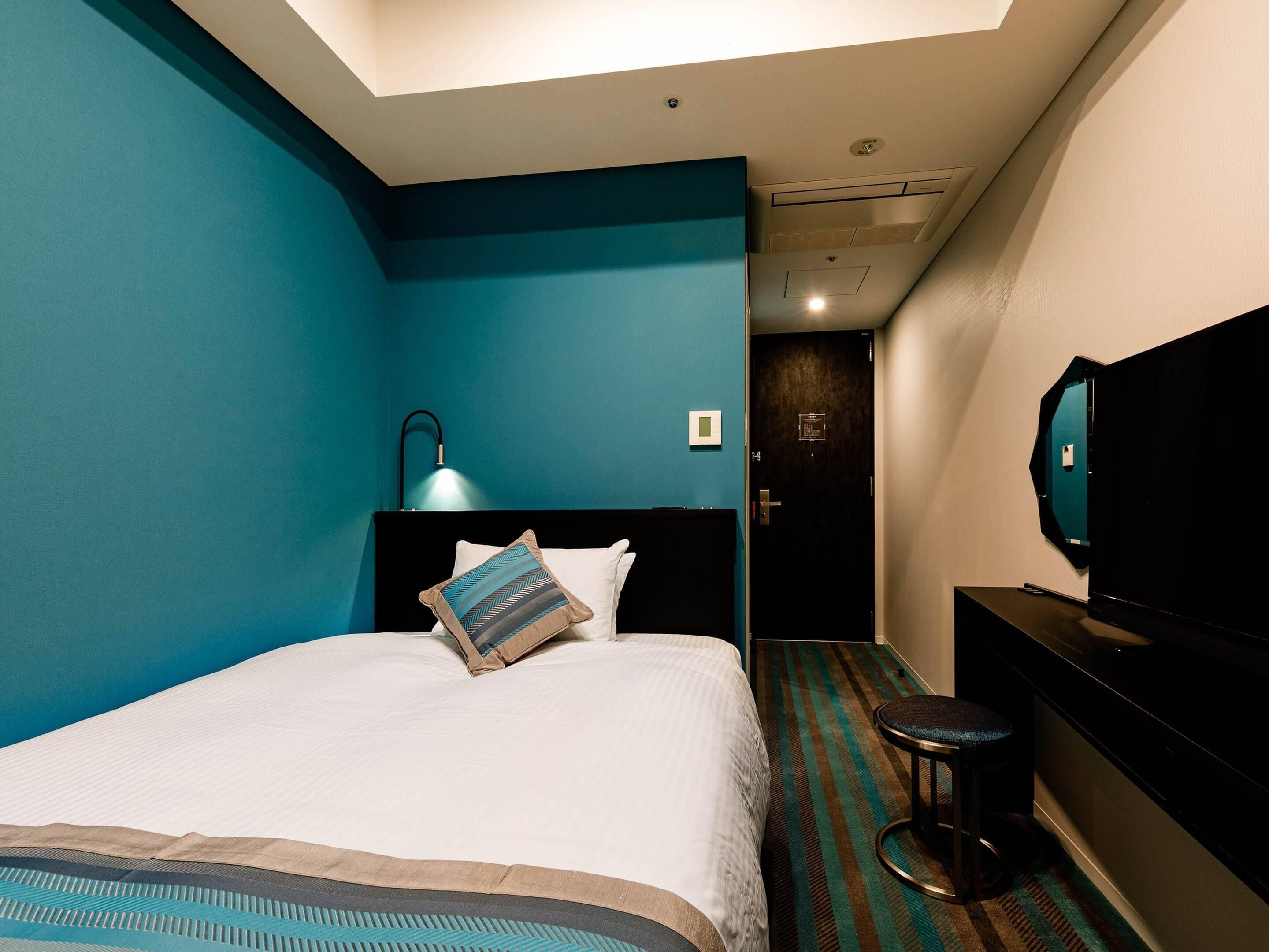 A hotel room with a bed, a desk, a chair, a TV, and a ceiling light.