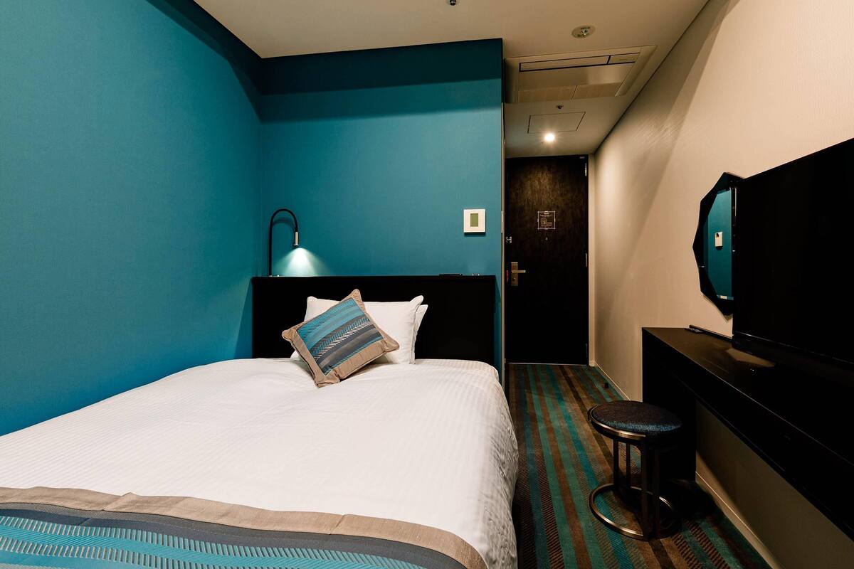 Une chambre d’hôtel équipée d’un lit, d’un bureau, d’une chaise, d’une télévision et d’un luminaire au plafond.