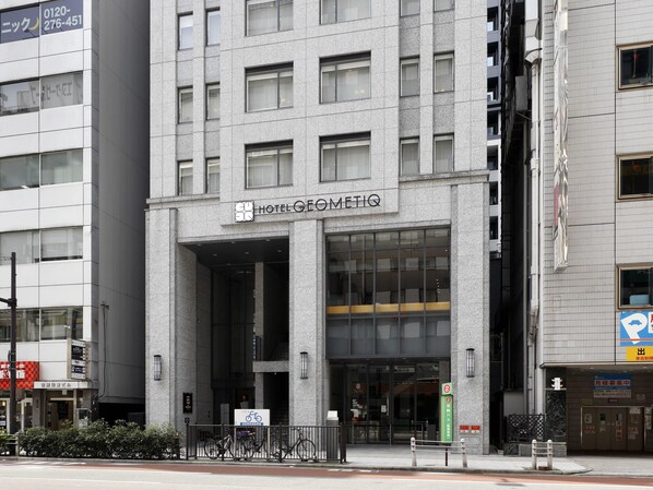 L’entrée d’un hôtel, avec une façade moderne, de grandes fenêtres et un panneau indiquant un espace de stationnement pour vélos.
