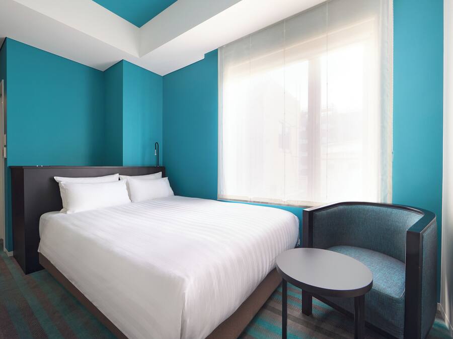 A hotel room with a bed, a chair, and a small table.