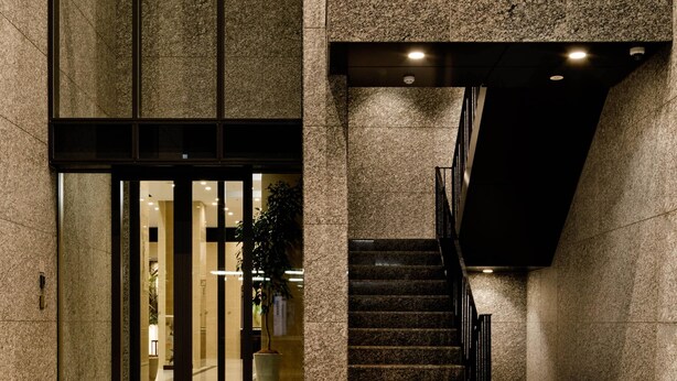 Entrada de un edificio con puerta de cristal, escalera y planta en maceta.