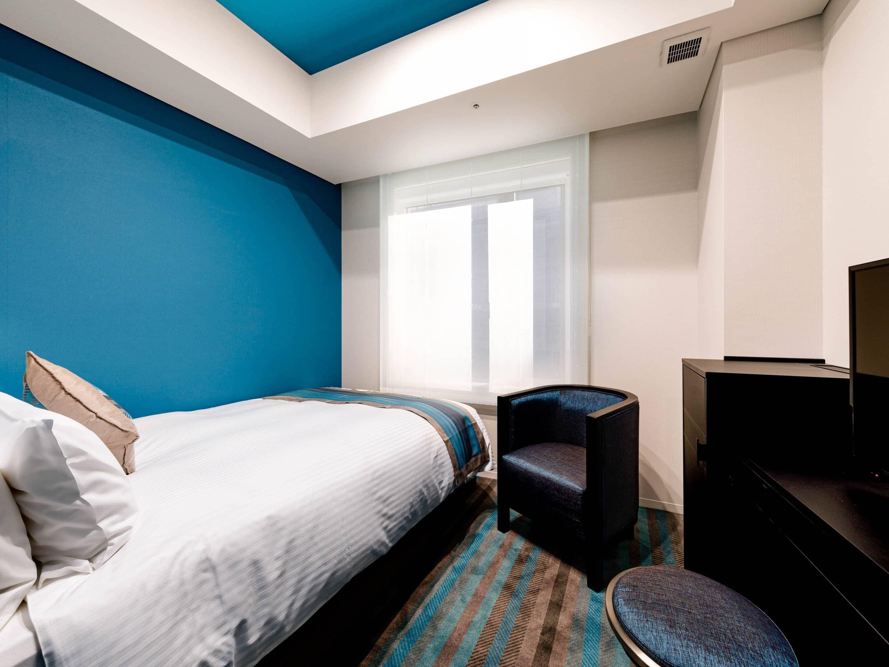 A hotel room with a bed, a chair, a desk, and a television.