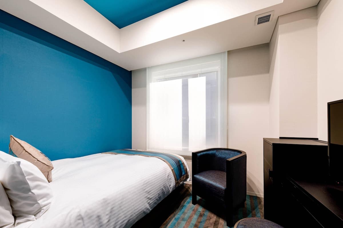 Une chambre d’hôtel avec un lit, une chaise, un bureau et un téléviseur.