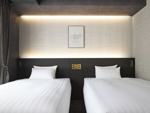 Une chambre d’hôtel avec deux lits, un tableau encadré au mur et un luminaire moderne au-dessus des lits.