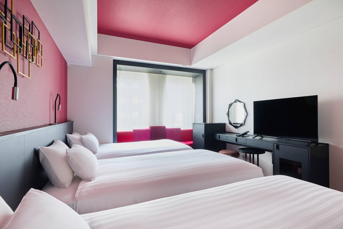 Een hotelkamer met twee bedden, een bureau, een televisie en een groot raam.