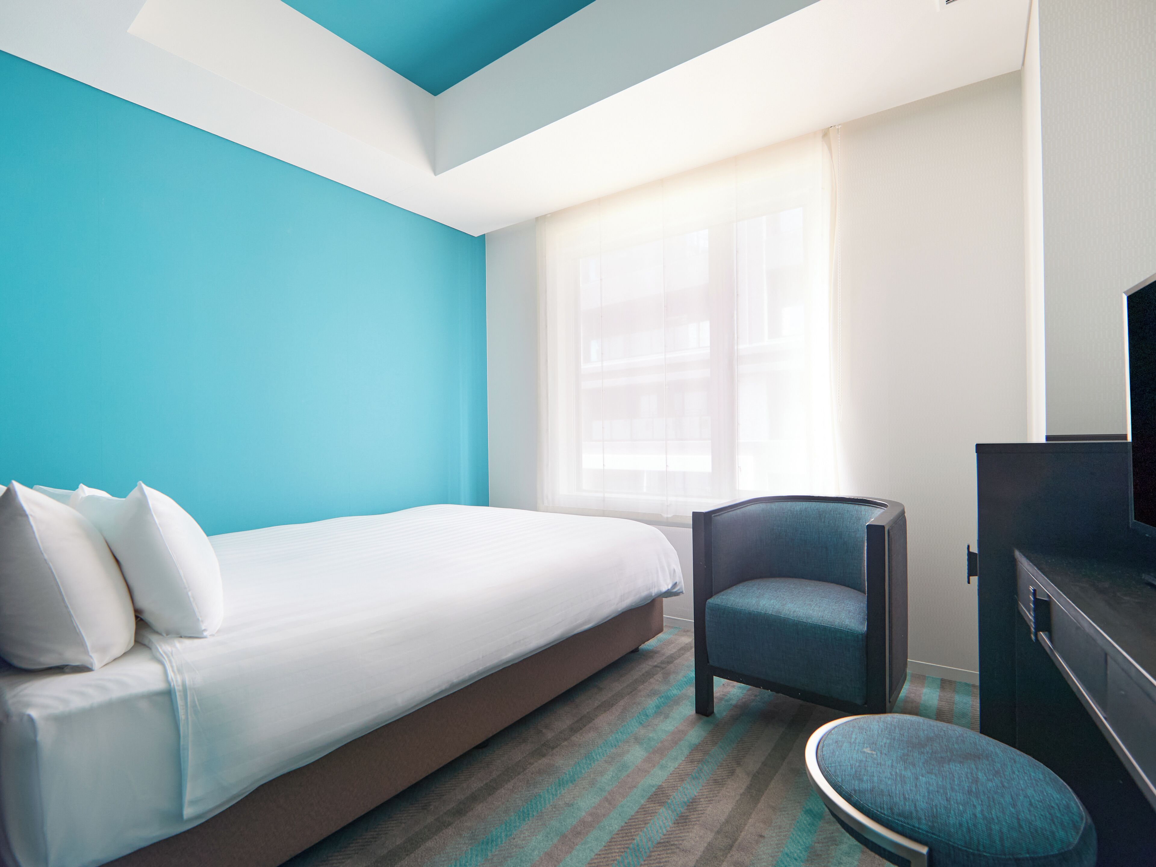 A hotel room with a bed, a chair, a television, and a window with curtains.