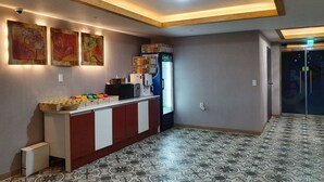 A hotel lobby with a reception desk, artwork on the walls, a refrigerator with beverages, and patterned floor tiles.