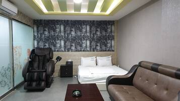 A hotel room with a bed, a massage chair, a massage table, a small table, and a wall with a cityscape mural.