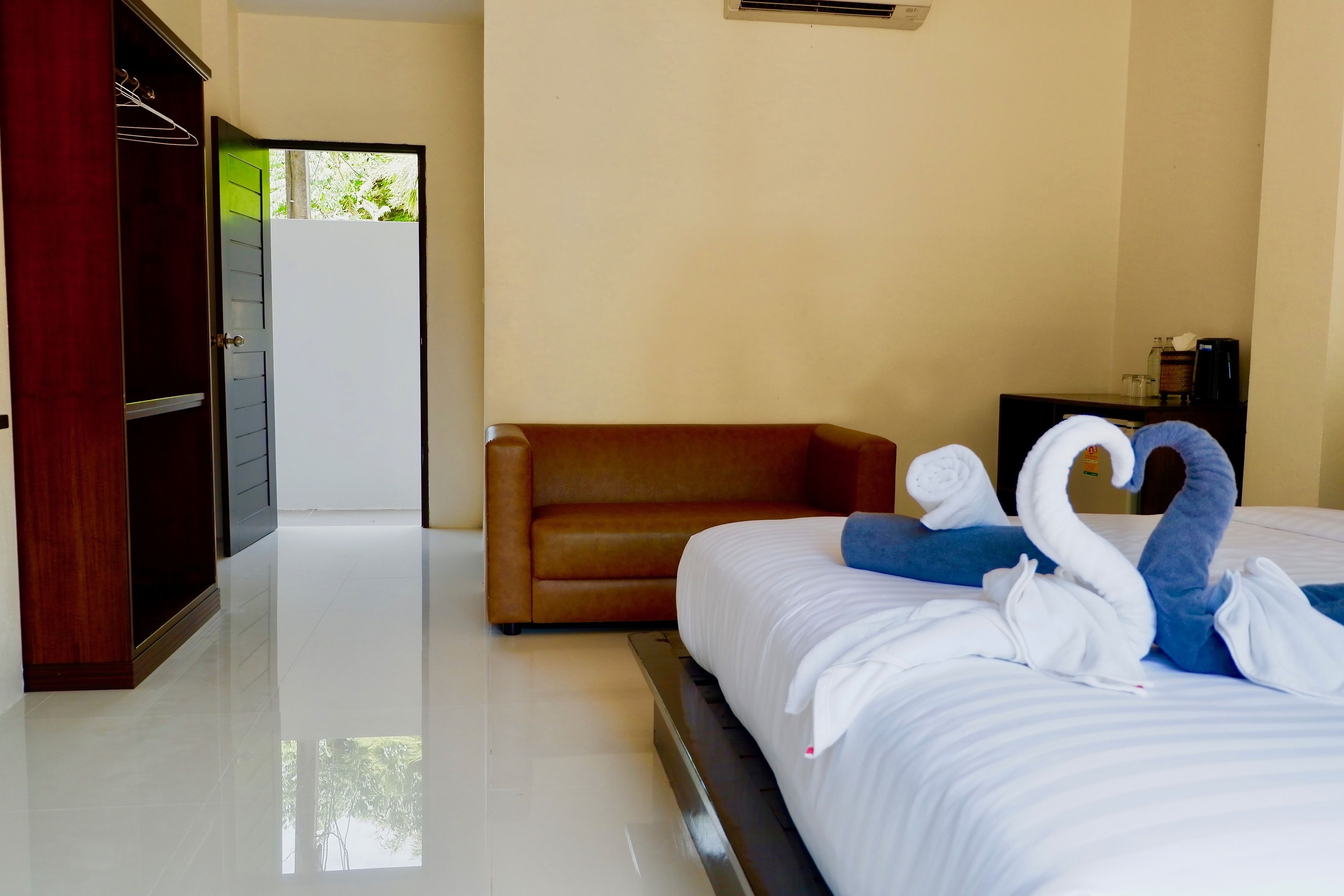 A hotel room with a bed, a brown sofa, a wardrobe, and a wall-mounted air conditioner.