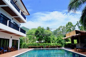 Un hotel moderno con piscina, asientos exteriores y abundante vegetación.
