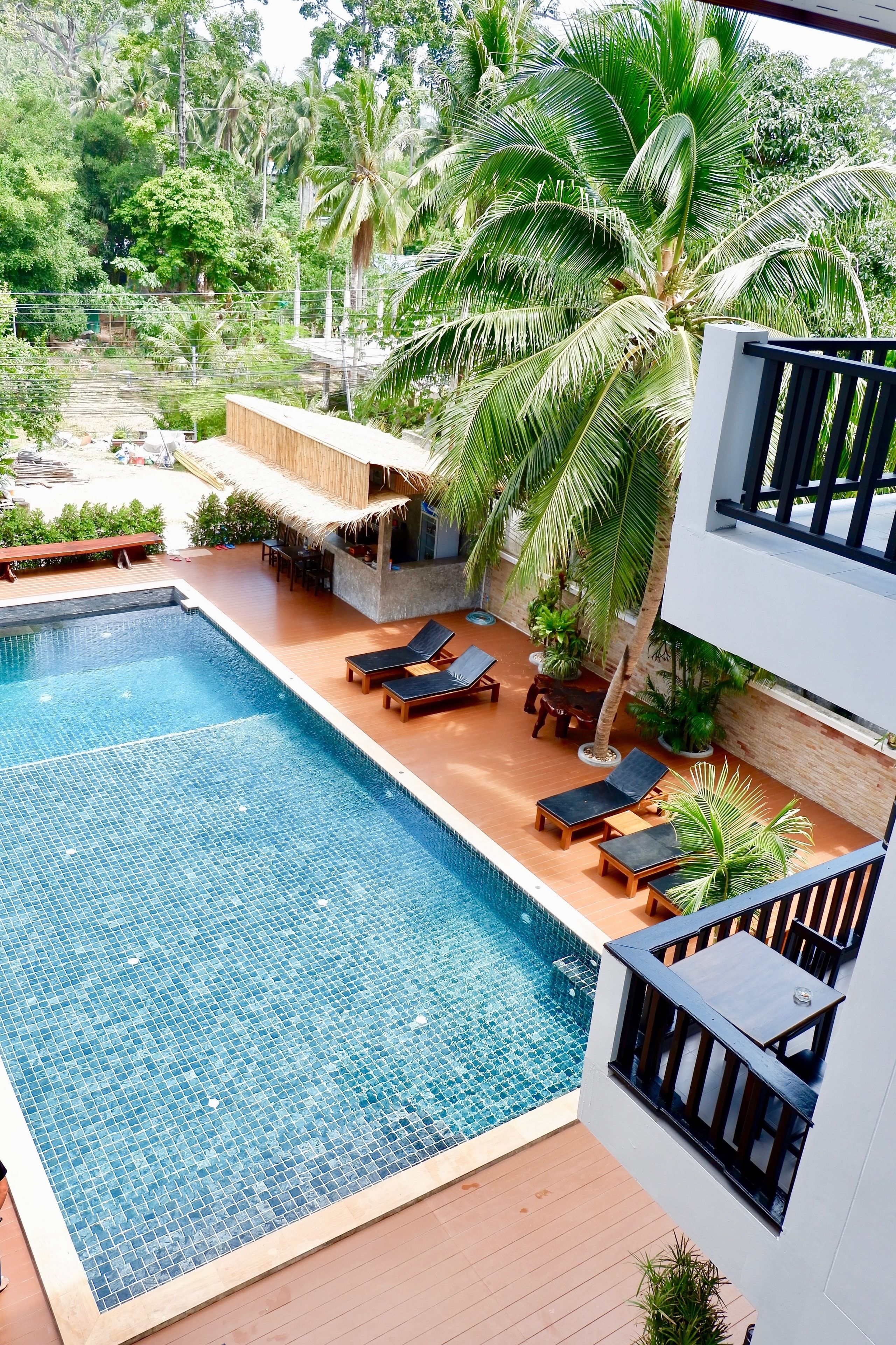 A swimming pool with lounge chairs and a thatched-roof structure surrounded by palm trees.