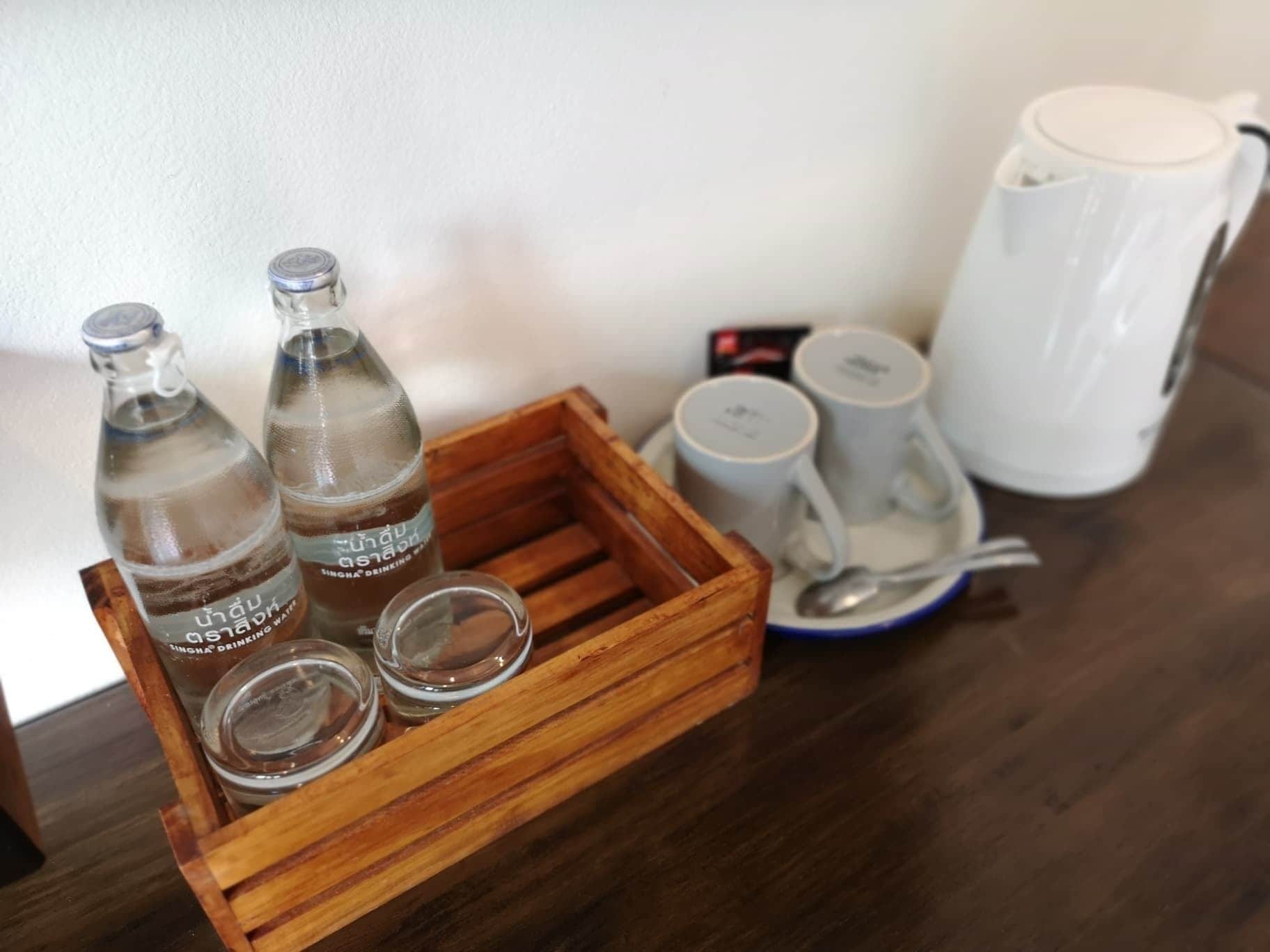 A wooden tray with three bottles and two empty glass containers, a white mug, and a tea kettle on a table.