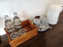 A wooden tray with three bottles and two empty glass containers, a white mug, and a tea kettle on a table.