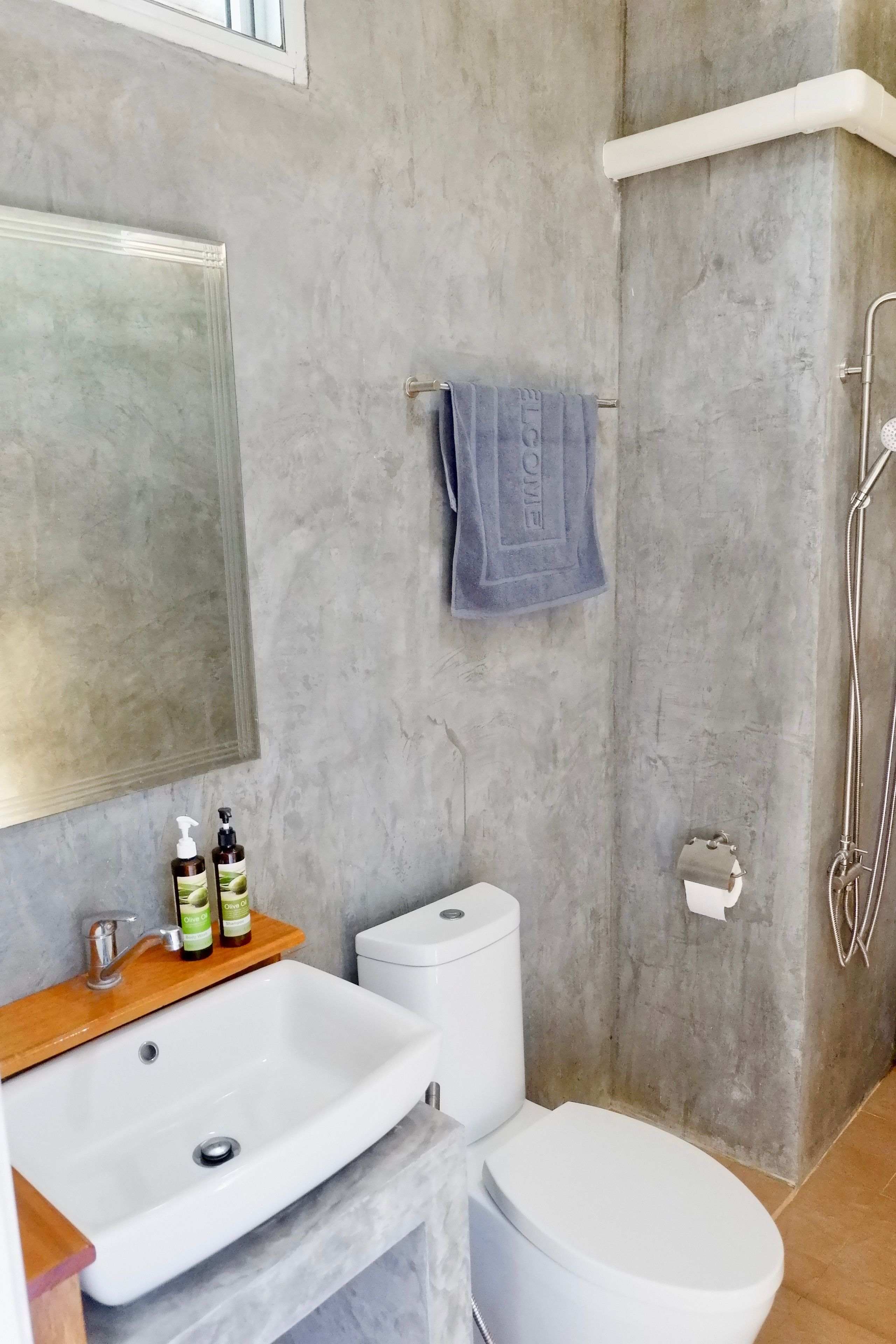 Un baño con un lavamanos blanco, un inodoro y una ducha. Hay una toalla colgada en la pared y un espejo sobre el lavamanos.