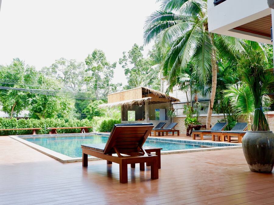 A wooden deck with a pool, lounge chairs, and a thatched-roof structure.