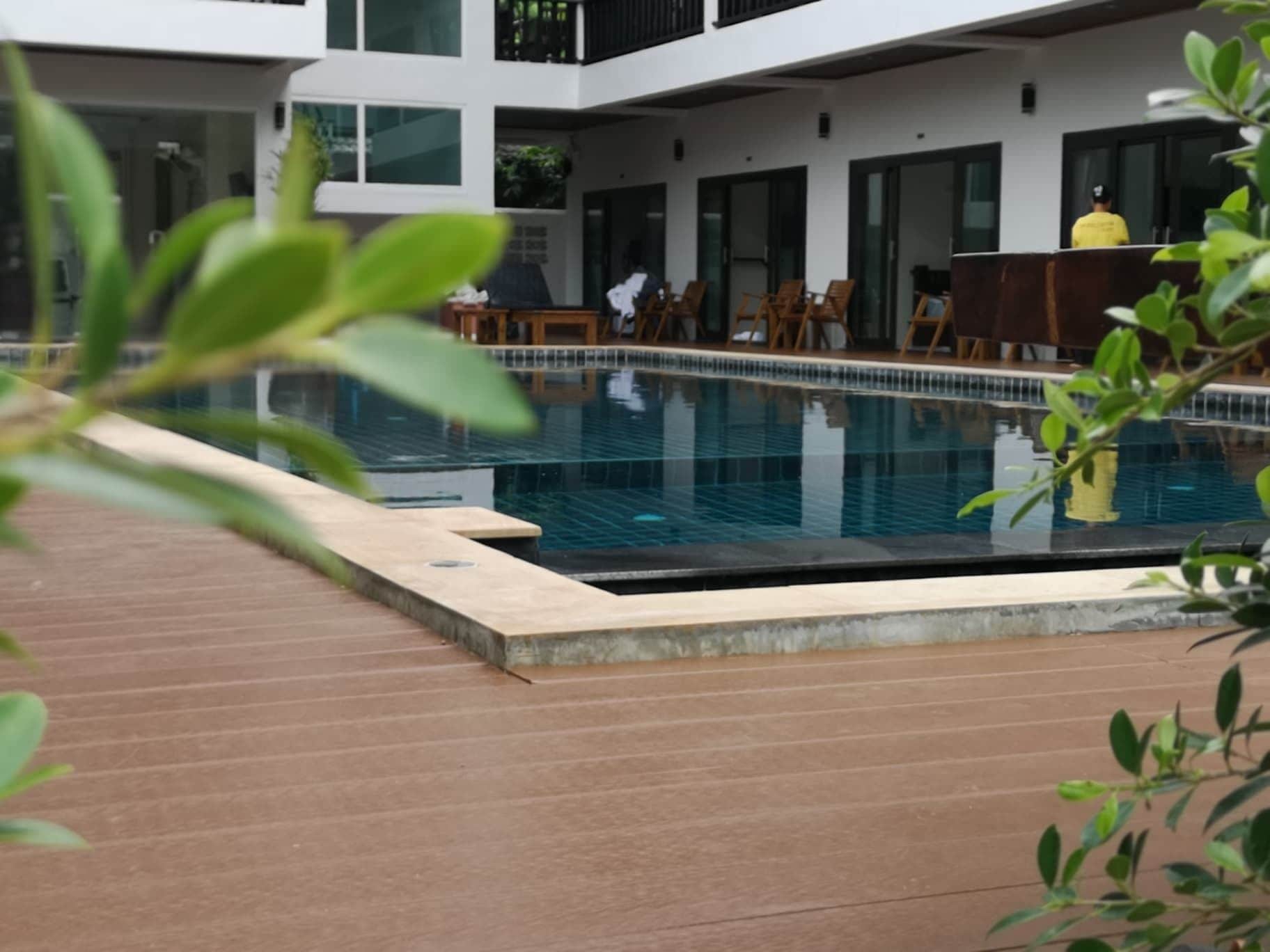 A modern pool area with a wooden deck, lounge chairs, and a person in a yellow uniform.