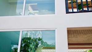 Un immeuble à plusieurs étages doté de grandes fenêtres, d’un balcon avec une balustrade et offrant une vue sur la verdure environnante.