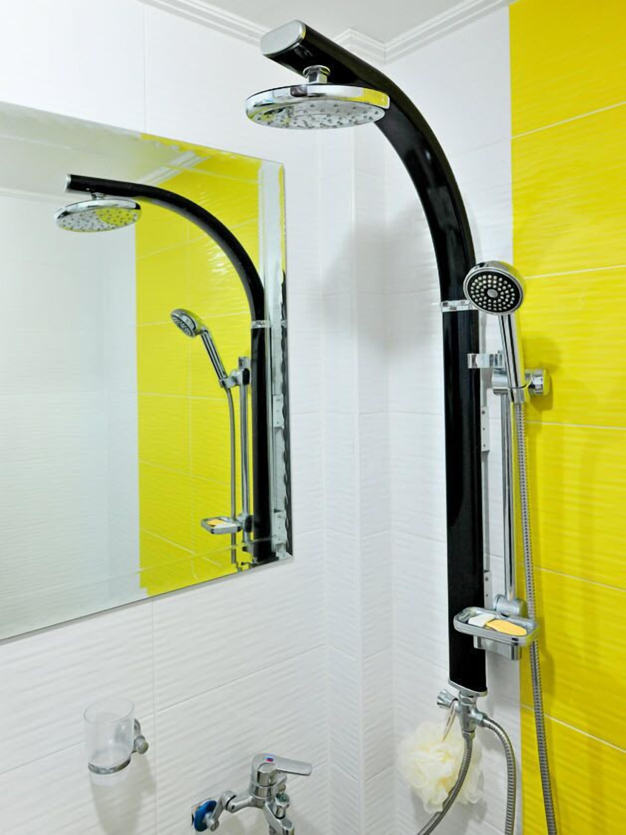 A bathroom with a yellow and white tiled wall, a chrome showerhead, and a handheld showerhead.