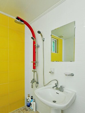 Un baño con azulejos amarillos y blancos, un lavamanos blanco, un espejo y un cabezal de ducha rojo.