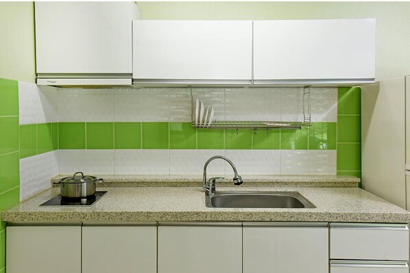 A kitchen with white cabinets, a granite countertop, a stainless steel sink, and a pot on an induction cooktop.